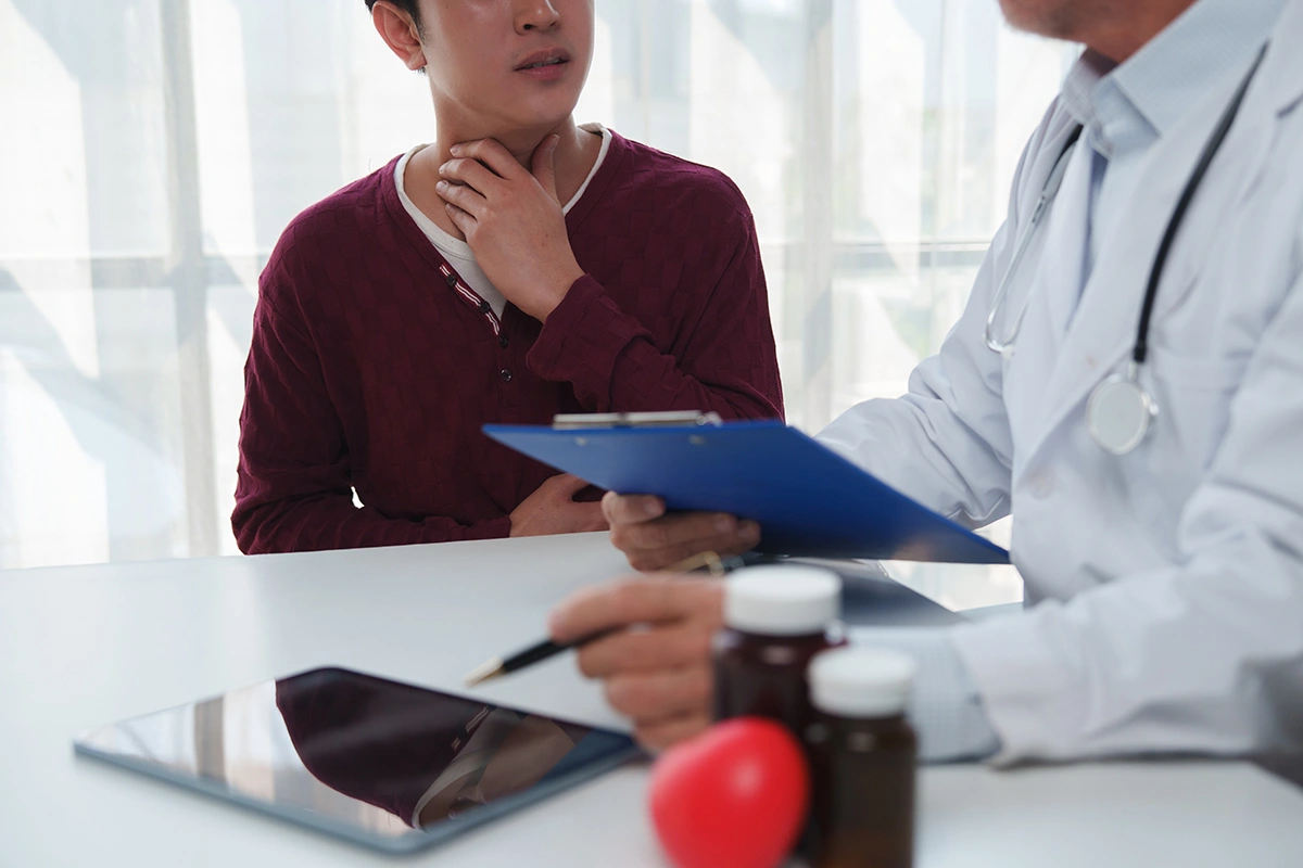 A man consulting a doctor for a sore throat that is possibly linked to acid reflux